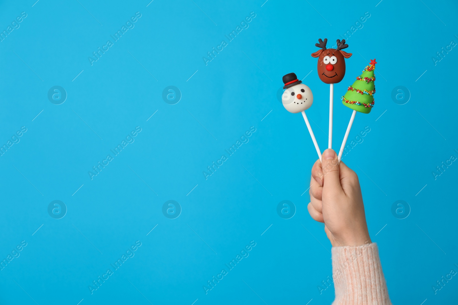 Photo of Woman holding delicious Christmas themed cake pops against light blue background, closeup. Space for text