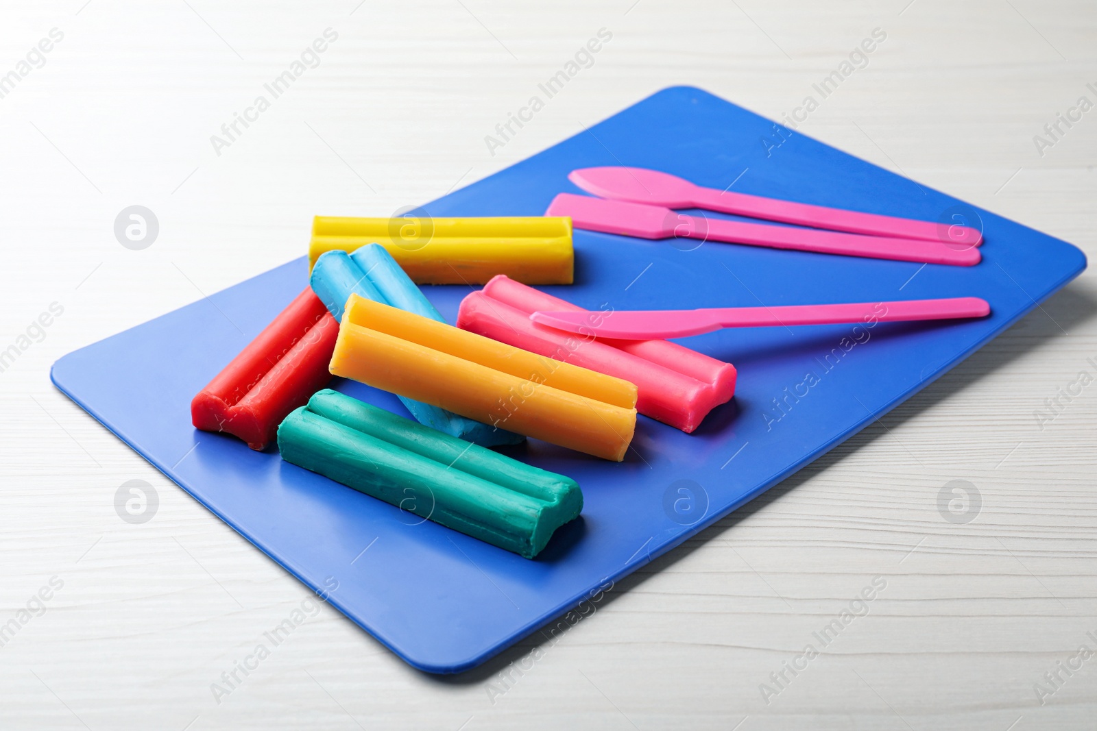 Photo of Many different colorful plasticine pieces with tools on white wooden table