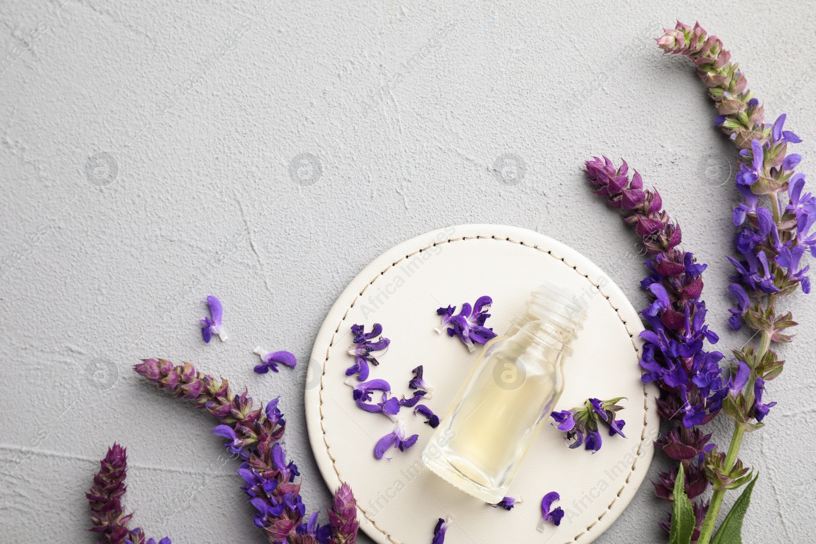 Photo of Bottle of sage essential oil and flowers on grey table, flat lay. Space for text