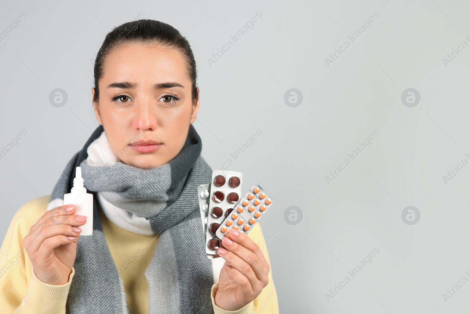 Photo of Woman with nasal spray and pills on light grey background, space for text