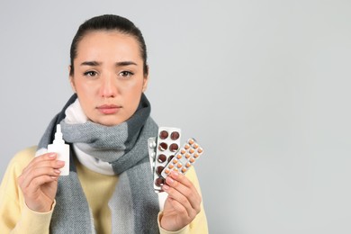 Woman with nasal spray and pills on light grey background, space for text