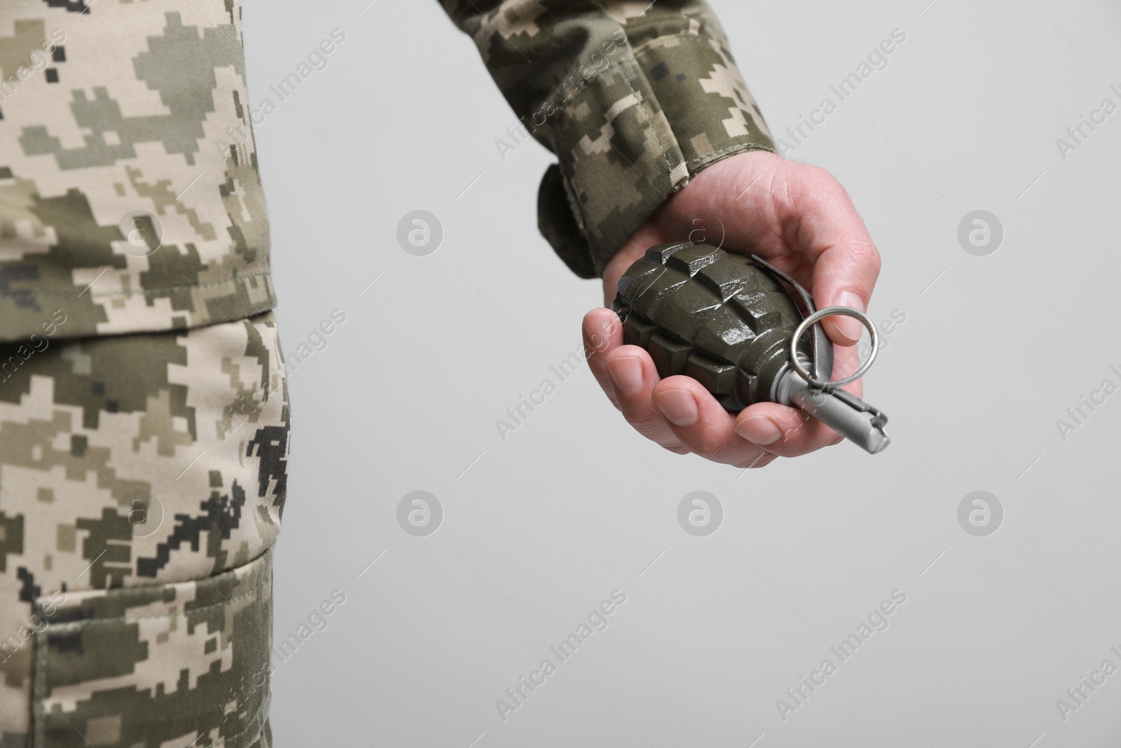 Photo of Soldier holding hand grenade on light grey background, closeup. Military service