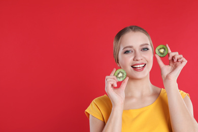 Photo of Young woman with cut kiwi on red background, space for text. Vitamin rich food