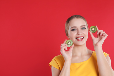 Young woman with cut kiwi on red background, space for text. Vitamin rich food