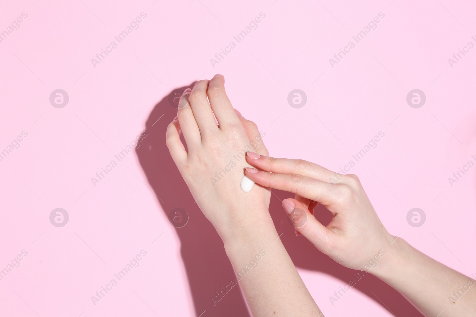 Photo of Woman applying cream on her hand against pink background, closeup