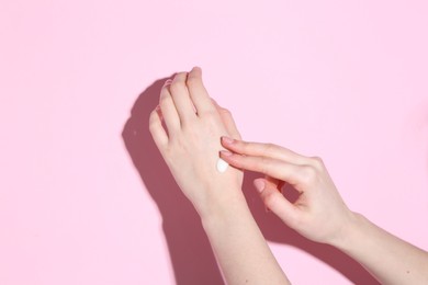 Photo of Woman applying cream on her hand against pink background, closeup