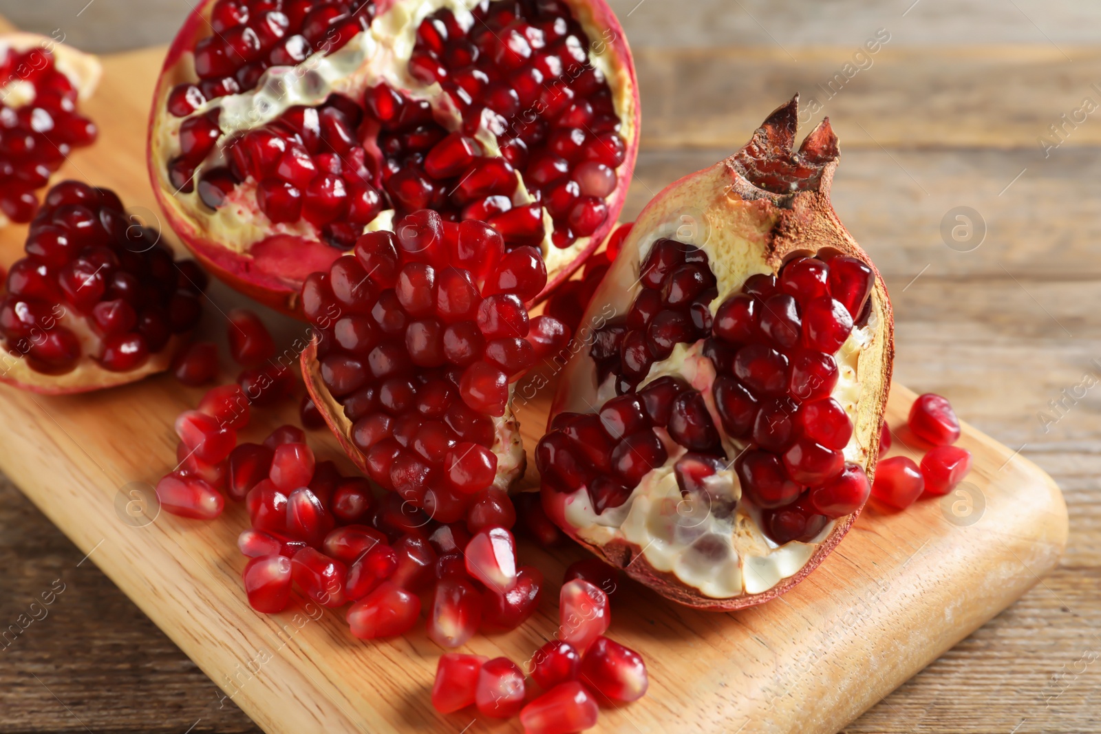 Photo of Ripe pomegranates and seeds on wooden board, closeup