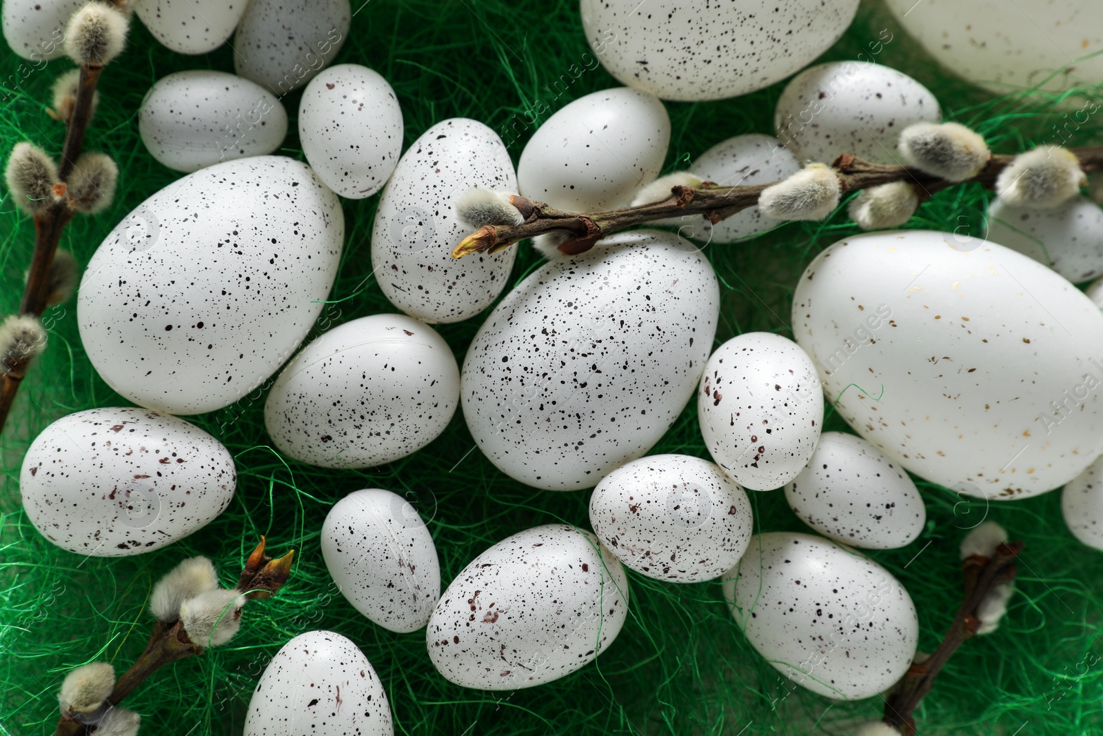 Photo of Many beautifully painted Easter eggs and pussy willow branches on green background, flat lay