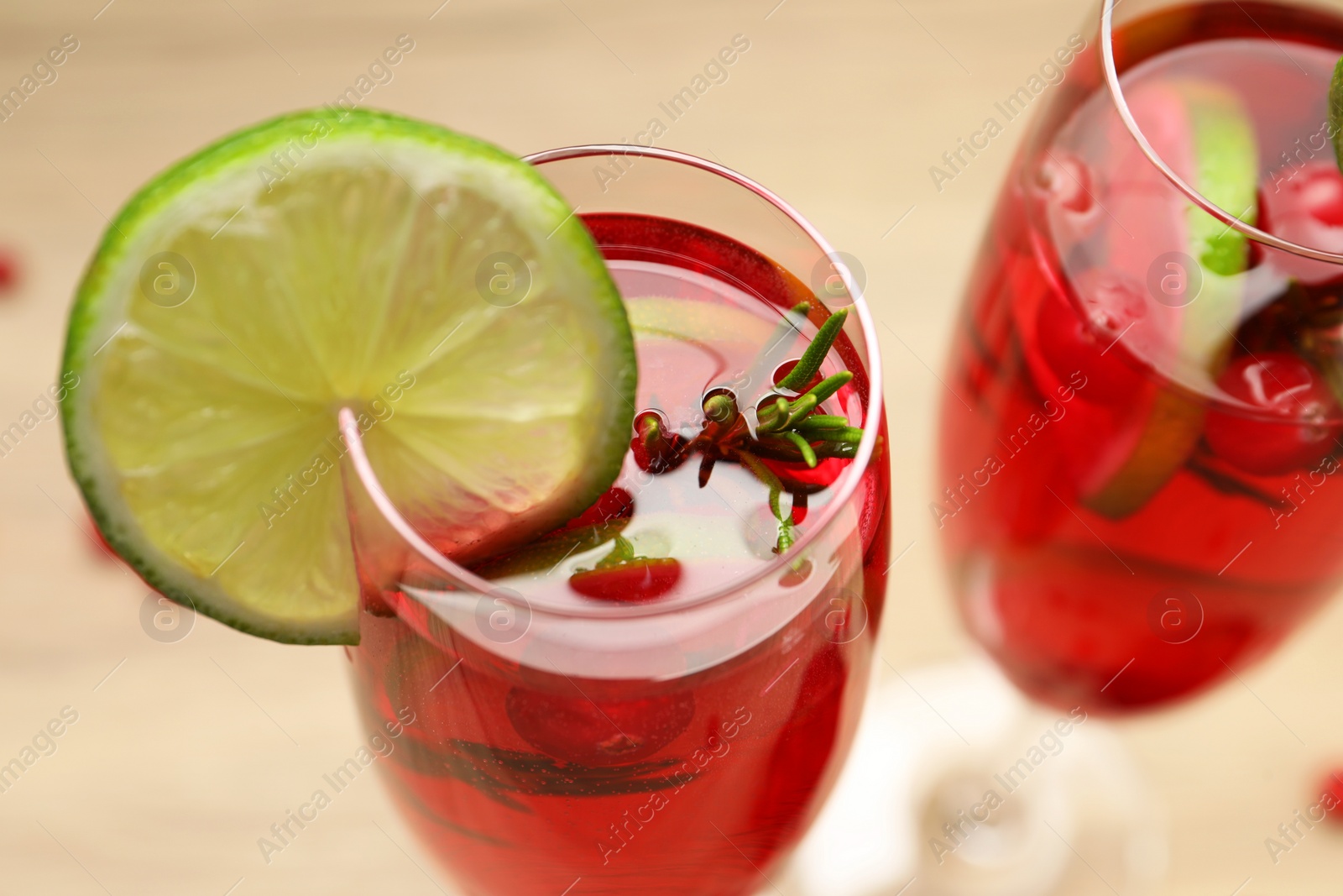 Photo of Tasty cranberry cocktail with rosemary and lime in glasses on beige table, closeup