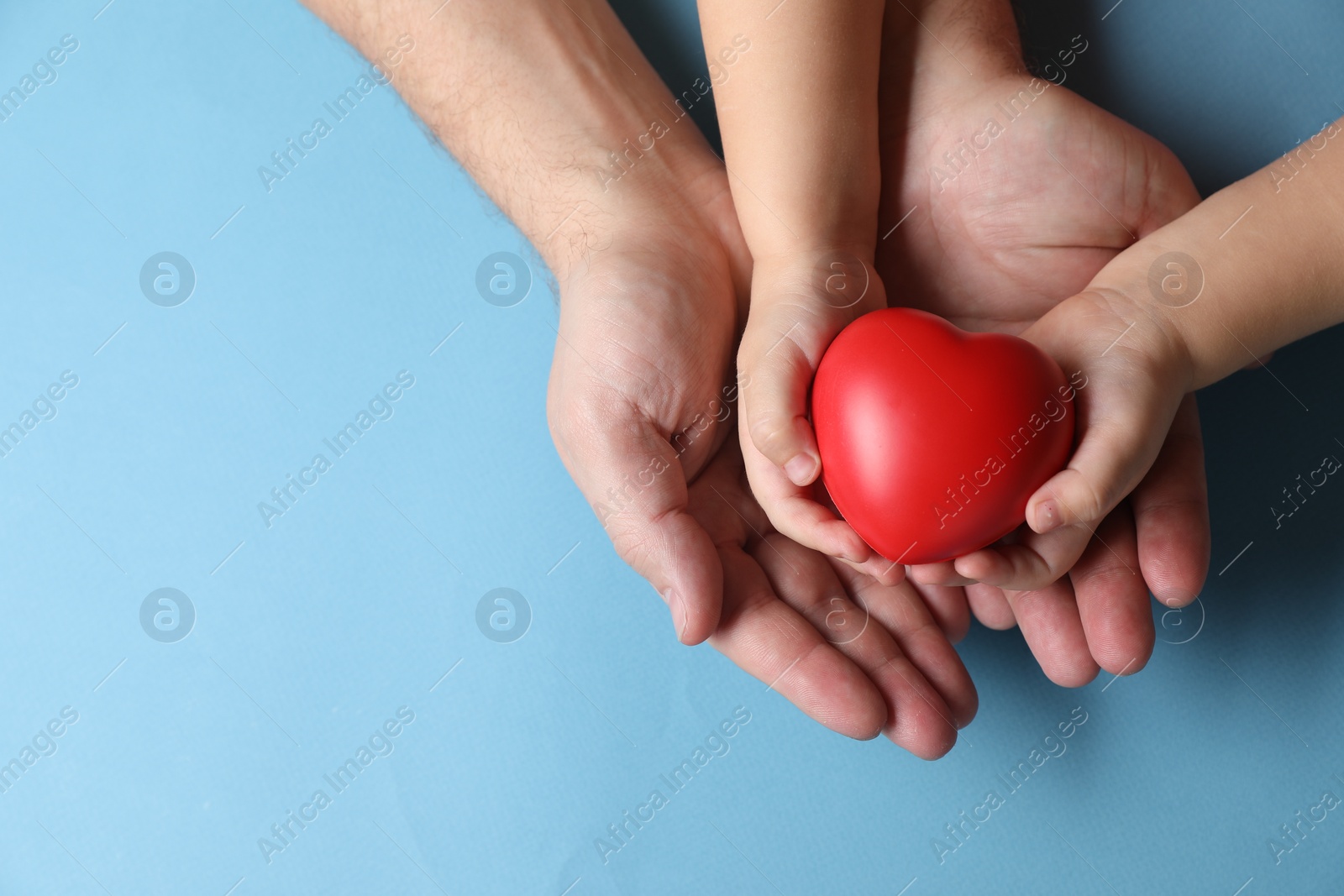 Photo of Father and his child holding red decorative heart on light blue background, top view. Space for text