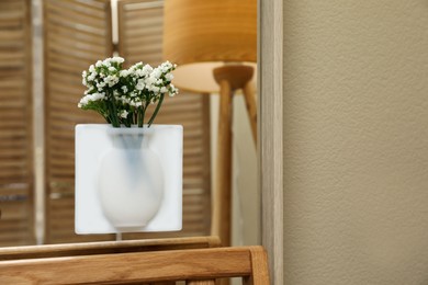 Photo of Silicone vase with beautiful white flowers on mirror in room, space for text