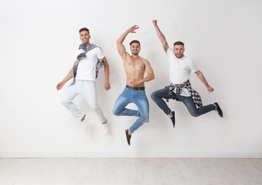 Group of young men in jeans jumping near light wall