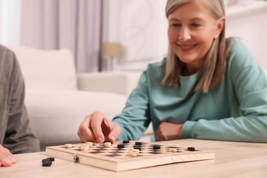 People playing checkers at wooden table in room, selective focus