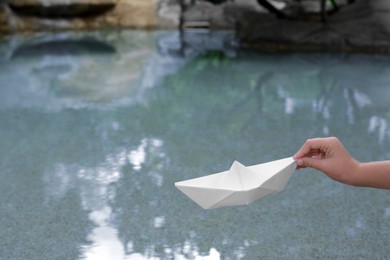 Kid launching small white paper boat on pond, closeup. Space for text