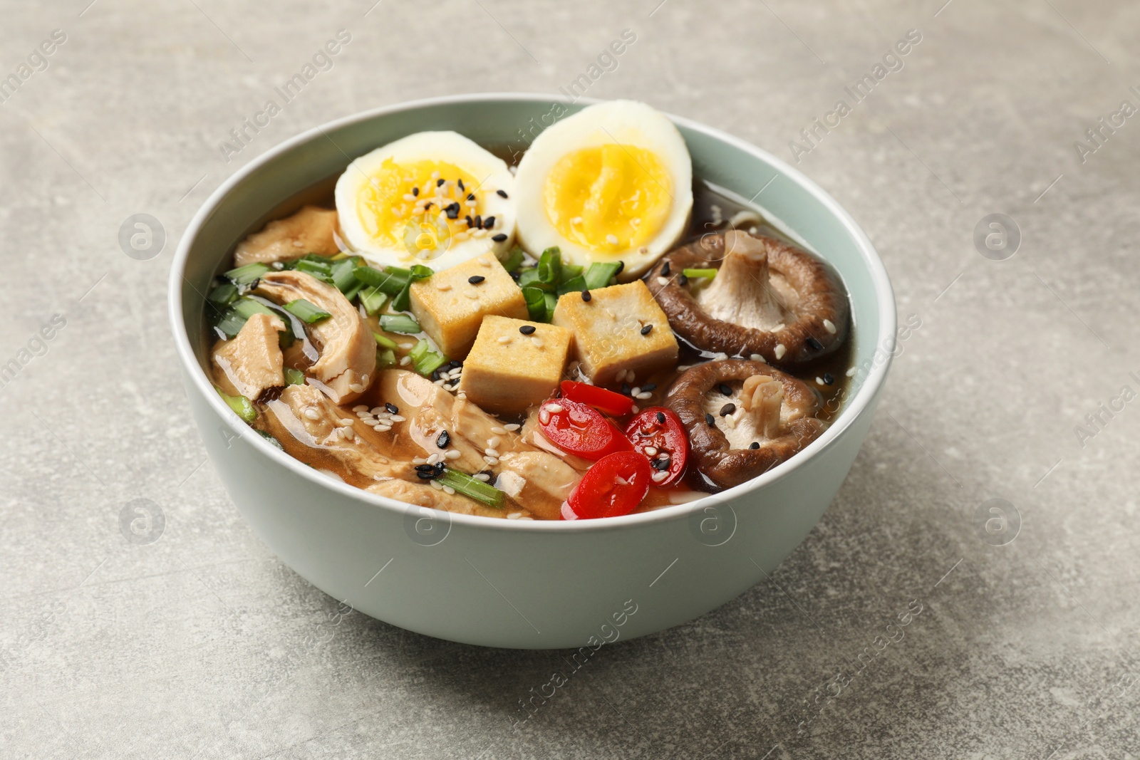 Photo of Bowl of delicious ramen on grey table. Noodle soup