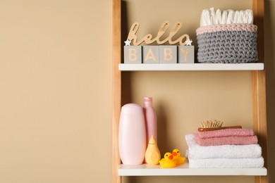 Photo of Towels, toys and baby accessories on wooden rack, space for text