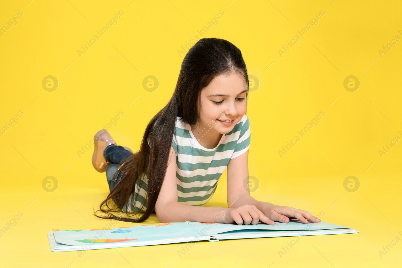 Photo of Cute little girl reading book on color background