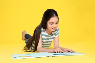 Cute little girl reading book on color background