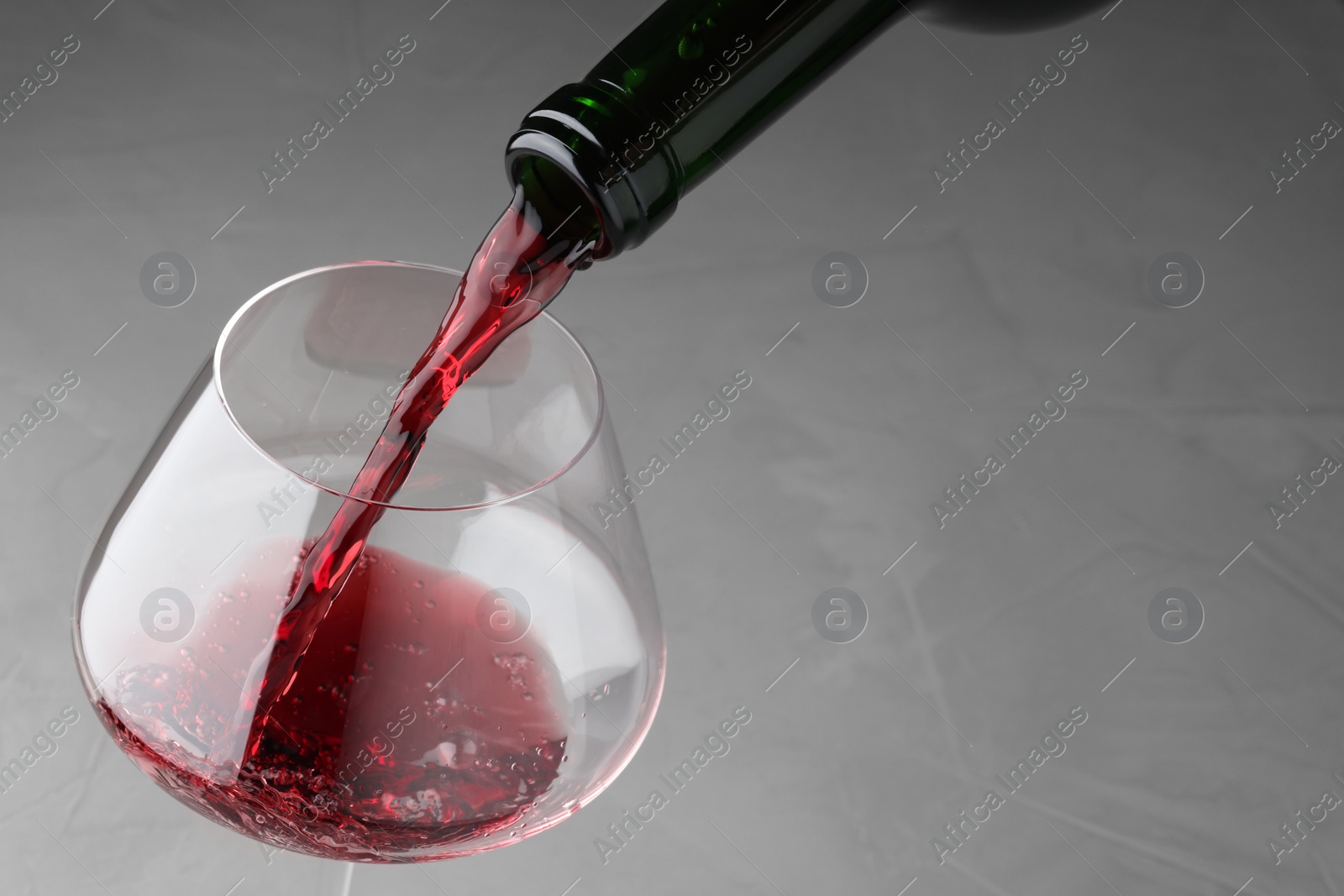 Photo of Pouring tasty red wine in glass at gray table, closeup. Space for text