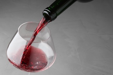 Pouring tasty red wine in glass at gray table, closeup. Space for text