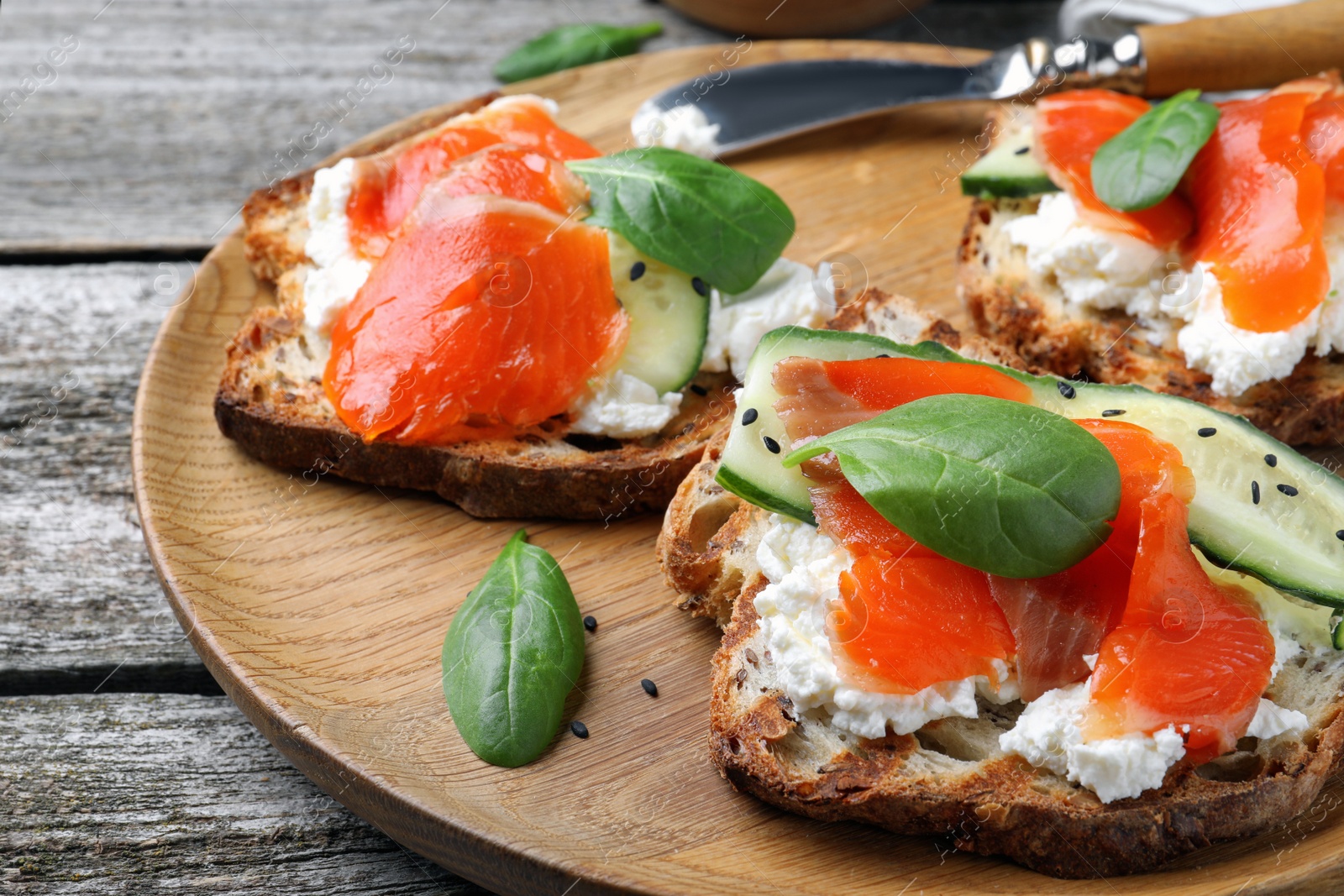 Photo of Delicious sandwiches with cream cheese, salmon, cucumber and spinach on wooden plate, closeup