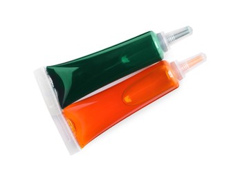 Tube with green and orange food coloring on white background, top view