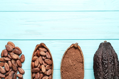 Photo of Cocoa beans, powder and pods on light blue table, flat lay. Space for text