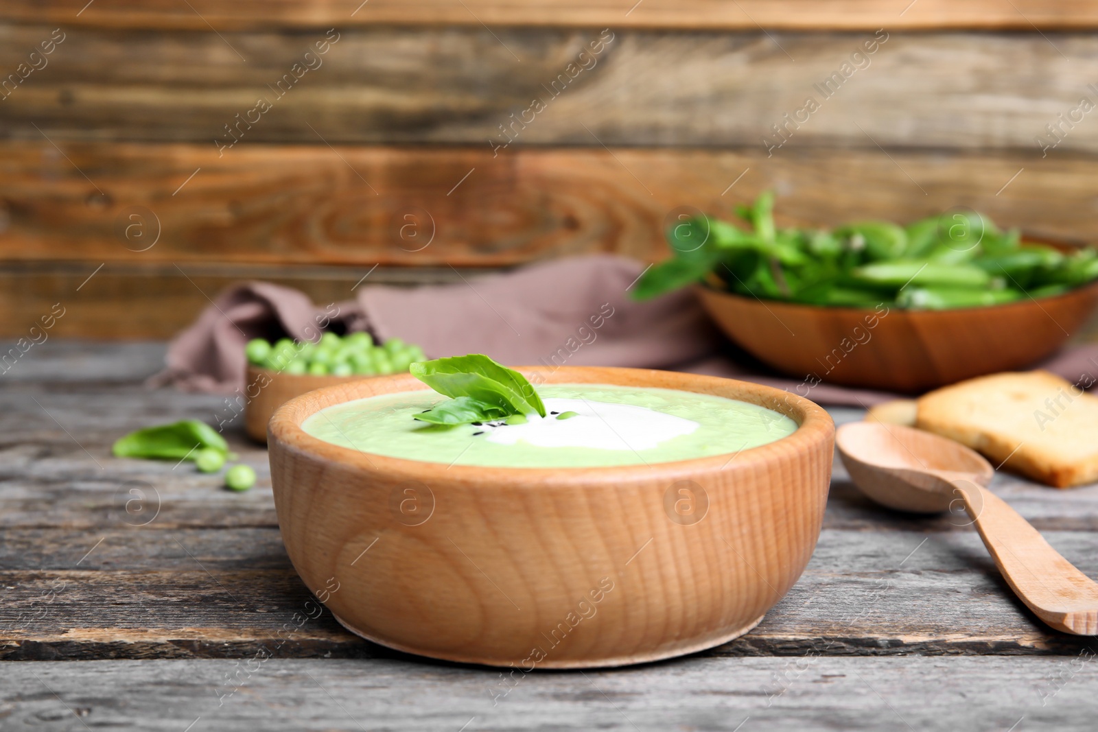 Photo of Green pea soup in bowl on wooden table