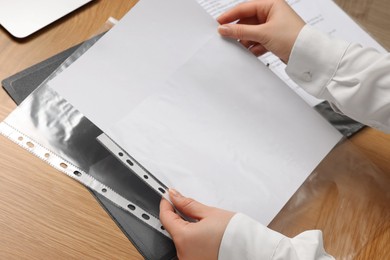 Photo of Woman putting paper sheet into punched pocket at wooden table, closeup