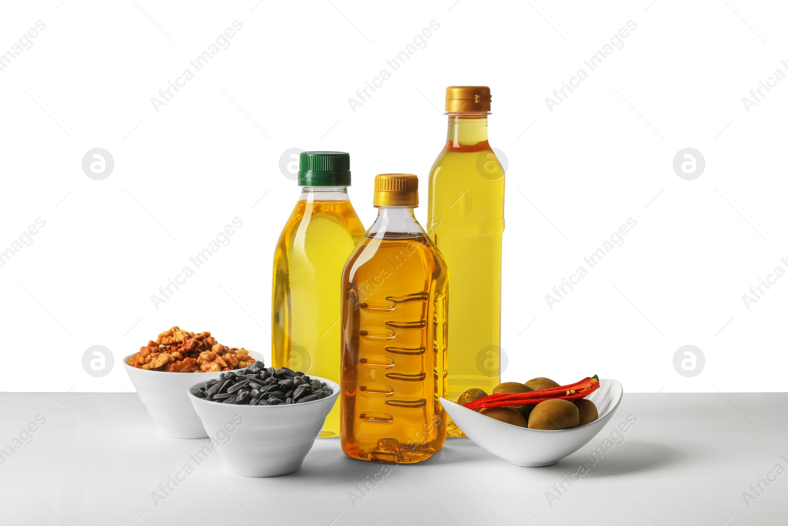 Photo of Bottles of different cooking oils, sunflower seeds, walnuts and olives on white background