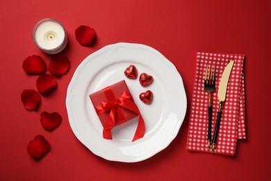 Photo of Beautiful table setting with gift box and rose petals dinner on red table for romantic, flat lay