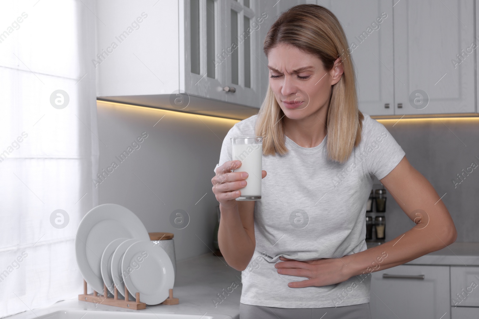 Photo of Woman with glass of milk suffering from lactose intolerance in kitchen, space for text