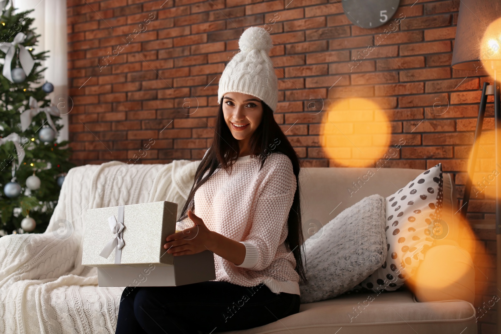 Photo of Beautiful young woman in hat opening gift box at home. Christmas celebration