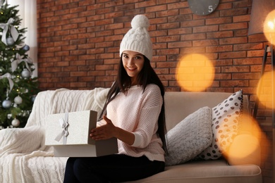 Photo of Beautiful young woman in hat opening gift box at home. Christmas celebration