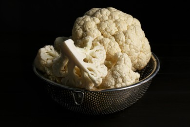 Photo of Colander with fresh raw cauliflower on black wooden table