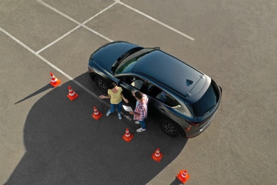 Photo of Instructor with clipboard near car and his student outdoors, above view. Driving school exam