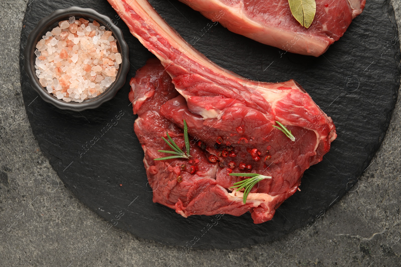 Photo of Pieces of raw beef meat and spices on grey textured table, top view