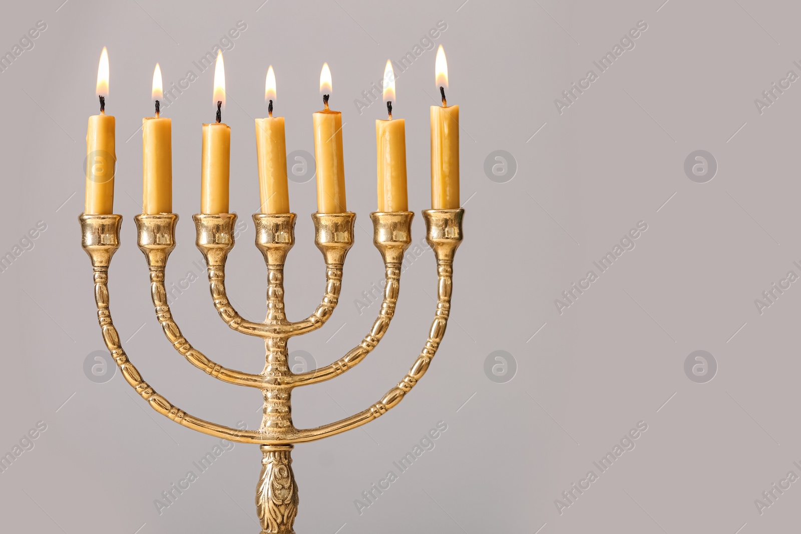 Photo of Golden menorah with burning candles on light grey background, space for text