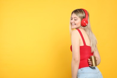 Beautiful happy woman holding beverage can on yellow background. Space for text