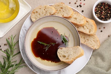 Bowl of balsamic vinegar with oil, rosemary, bread slices and spices on table, flat lay