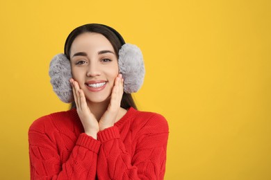 Beautiful young woman wearing earmuffs on yellow background. Space for text