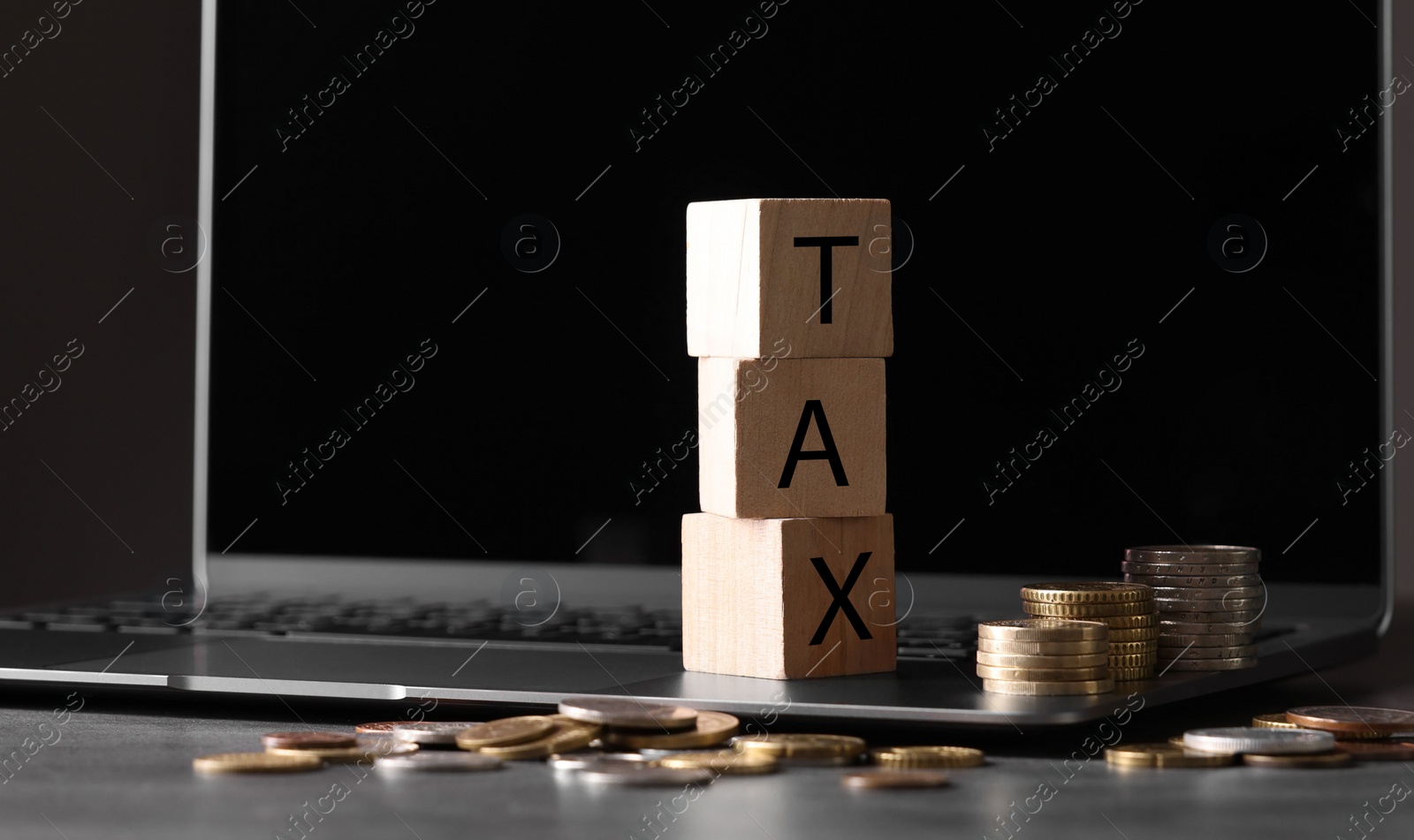 Photo of Word Tax made of wooden cubes, laptop and coins at grey table, space for text