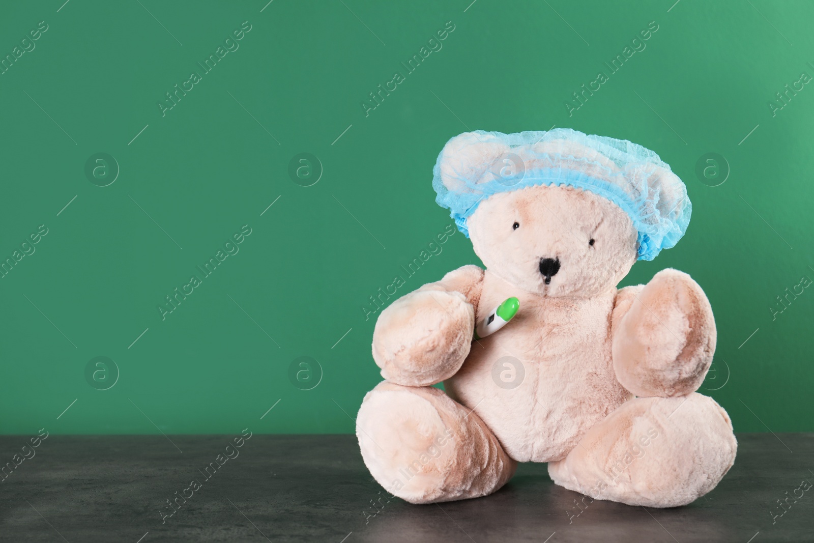 Photo of Toy bear with thermometer on table against color background, space for text. Children's hospital