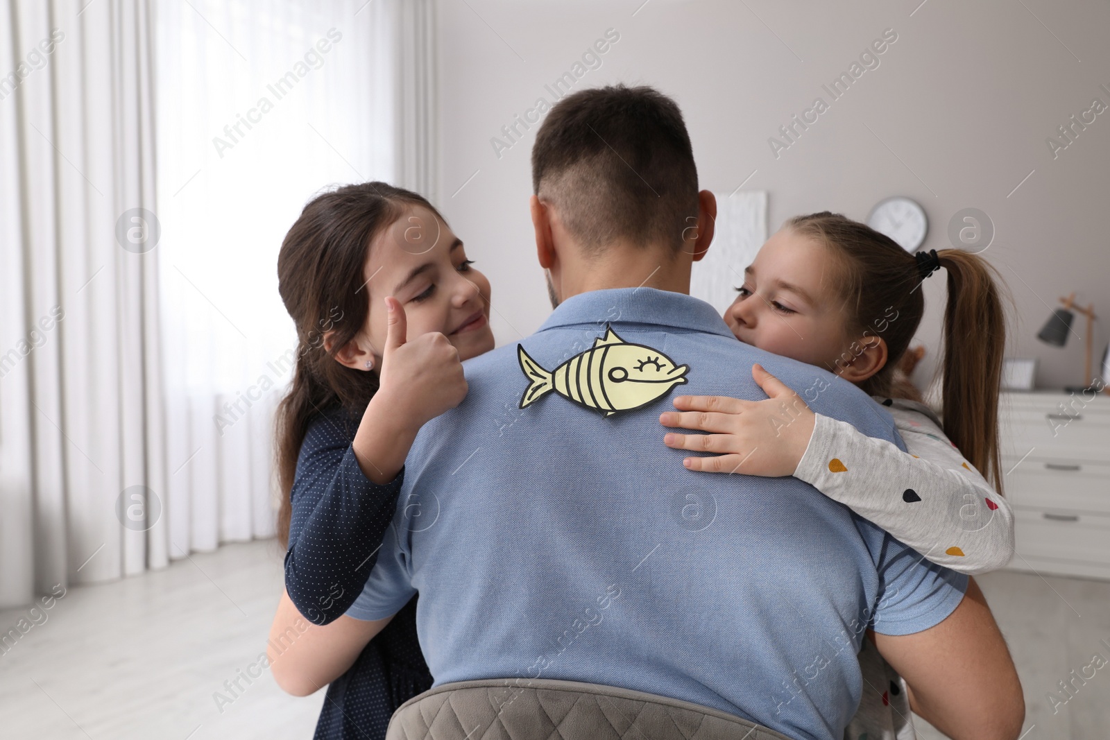 Photo of Cute little children sticking paper fish to father's back at home