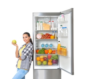 Young woman with apple near open refrigerator on white background