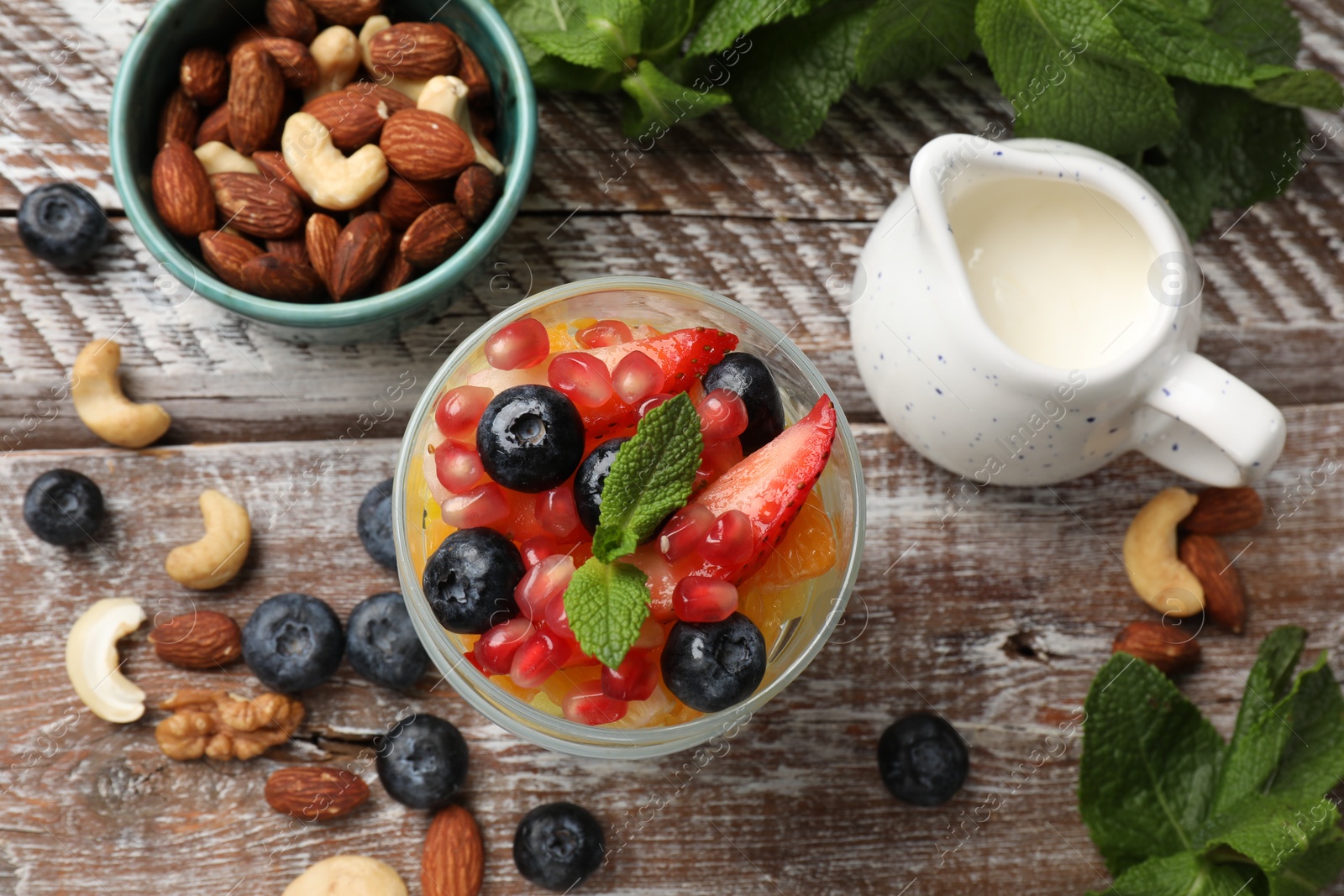 Photo of Delicious fruit salad, fresh berries, mint and nuts on wooden table, flat lay