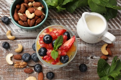 Delicious fruit salad, fresh berries, mint and nuts on wooden table, flat lay