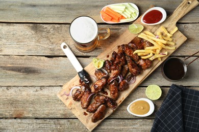 Photo of Tasty roasted chicken wings served with beer on wooden table, flat lay. Space for text