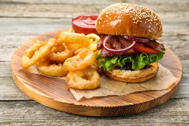 Photo of Tasty burger, fried onion rings and sauce on wooden table, closeup. Fast food