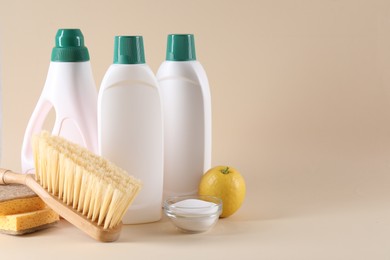 Photo of Bottles of cleaning product, sponges, brush, lemon and baking soda on beige background. Space for text